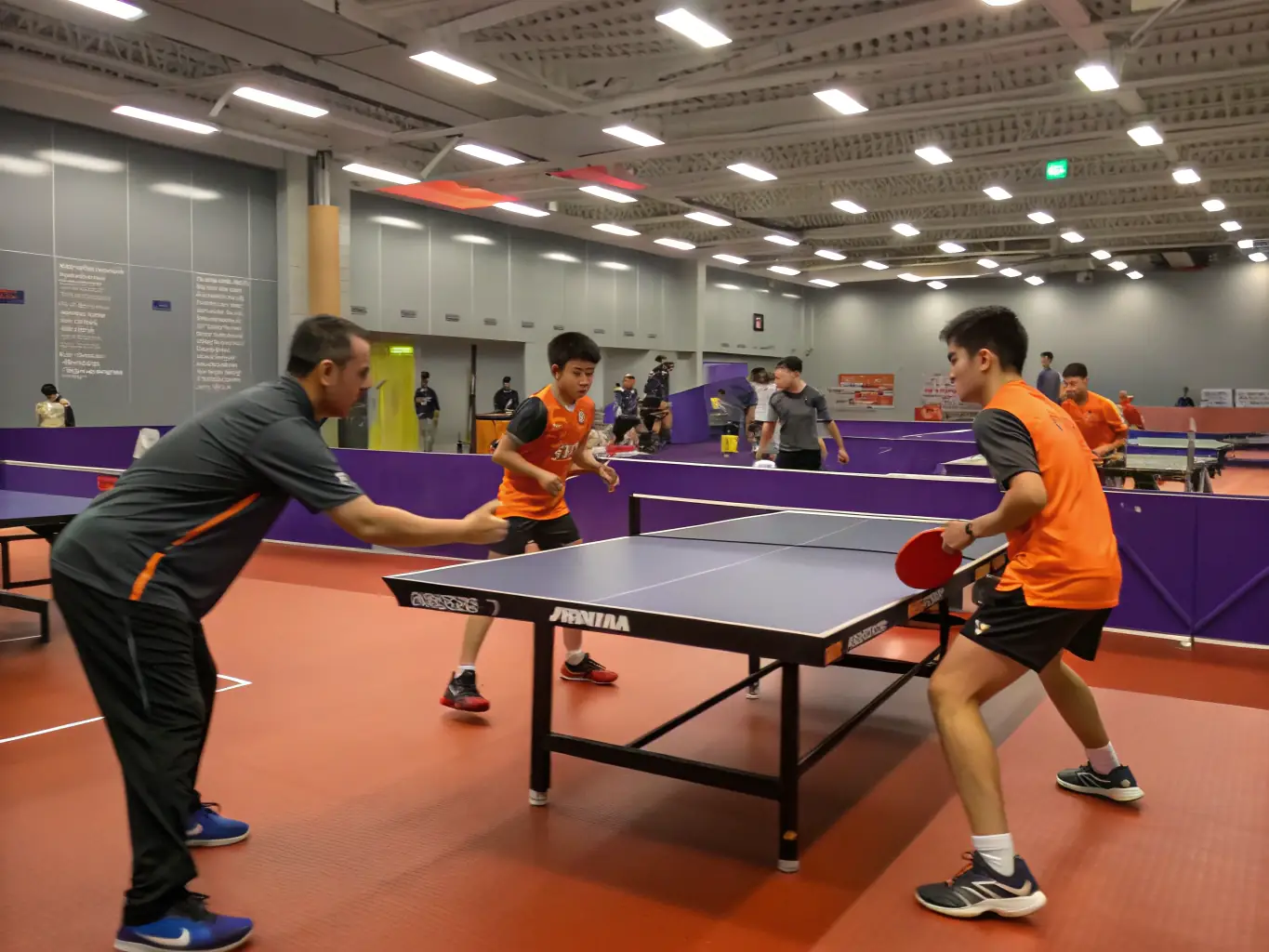 A group of children participating in a beginner's table tennis training session, focusing on basic strokes and techniques, with a coach providing guidance.